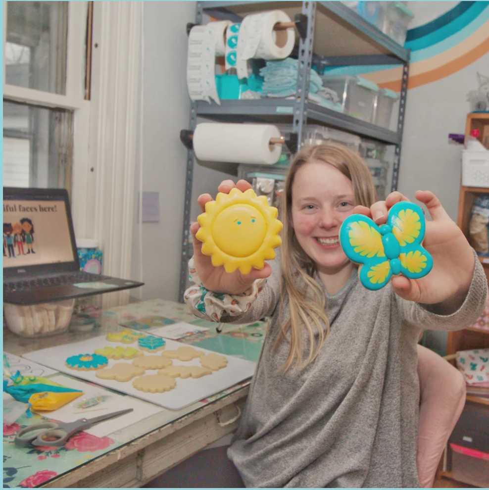 Virtual sugar cookie classes in Central Ma featuring Veronica the founder of The Cookie Lady's Daughter holding up two decorated sugar cookies.